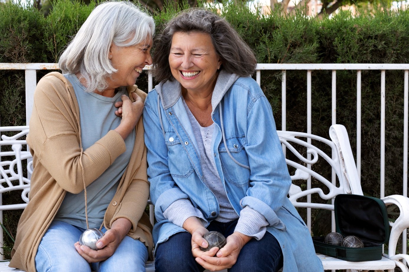 Zwei ältere Frauen lachen auf einer Bank – Joyspan im Ruhestand